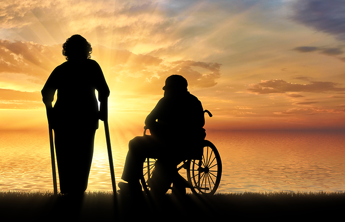 Silhouette of an old woman on crutches and elderly man in a wheelchair